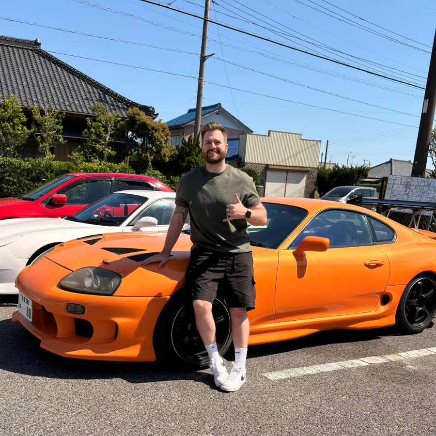Alex beside an orange Toyota Supra in Japan